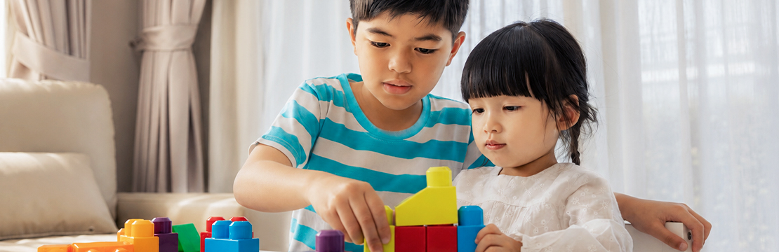Two siblings work together to build a structure with colorful blocks at a table, illustrating how sibling relationships help form the foundation of family connections and support.